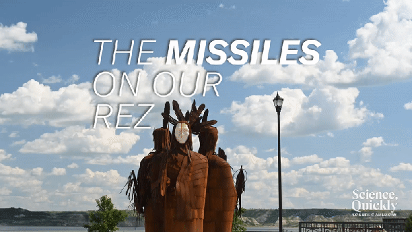 The statues of three Native American figures with headdresses stands amid a cloud filled sky below the text "The Missiles on Our Rez"