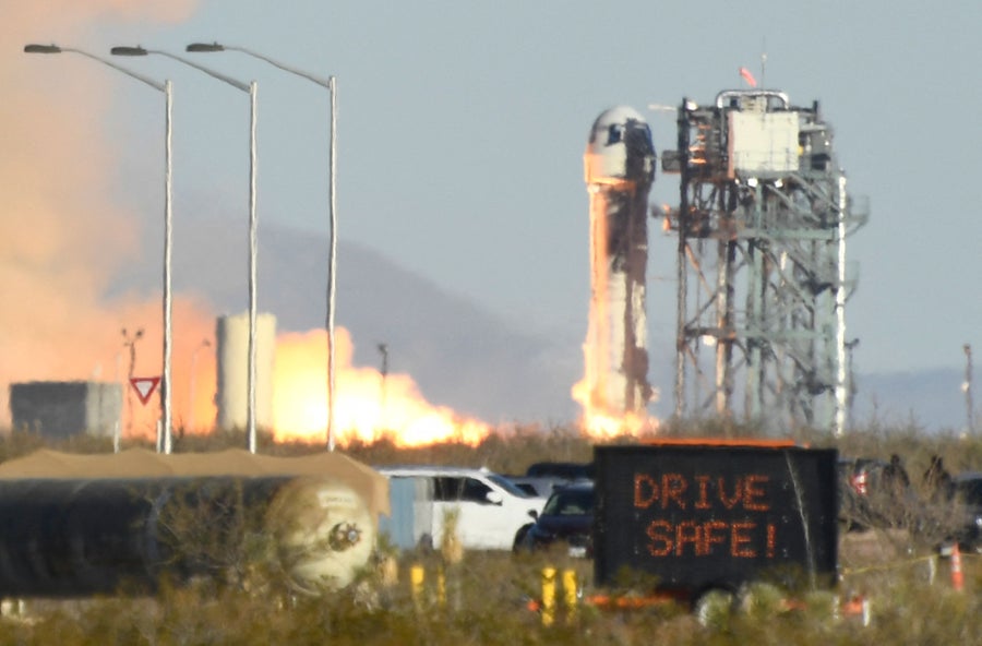 A digital traffic sign reads “DRIVE SAFE!” as a Blue Origin New Shepard rocket launches in the background in West Texas